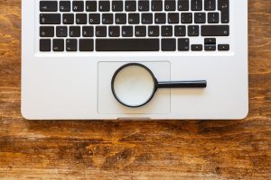 Magnifying glass on a computer laptop, wooden office desk background