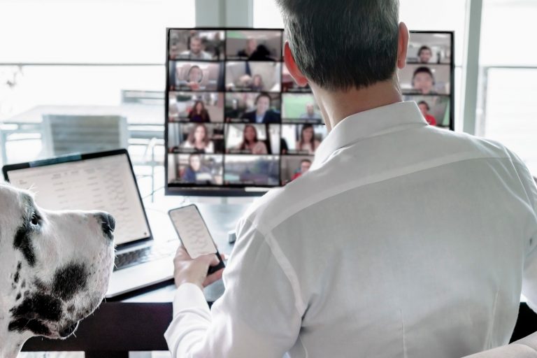 Man working remotely, multitasking video chatting with team and pet dog watching looking cute