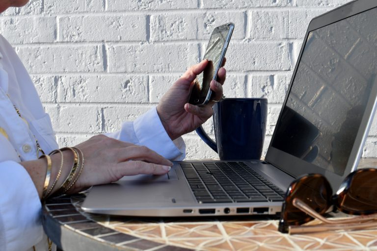 Professional business woman using a laptop & cellphone outside - multitasking