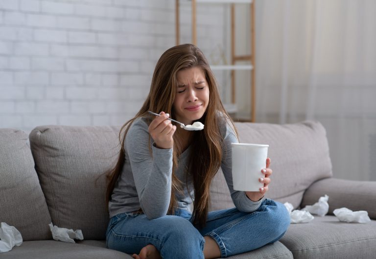 Sad millennial lady crying and eating ice cream while watching romantic movie after breakup